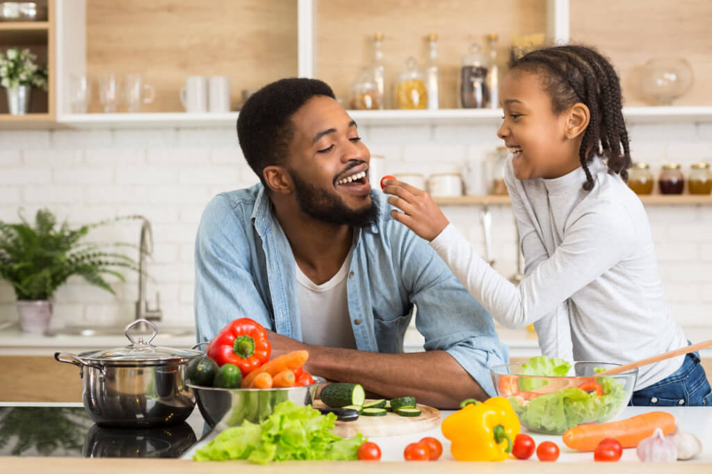 Daughter feeding her dad some vegetables while making a salad