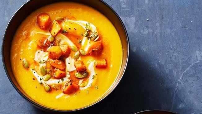 a bowl of squash soup next to a plate of bread