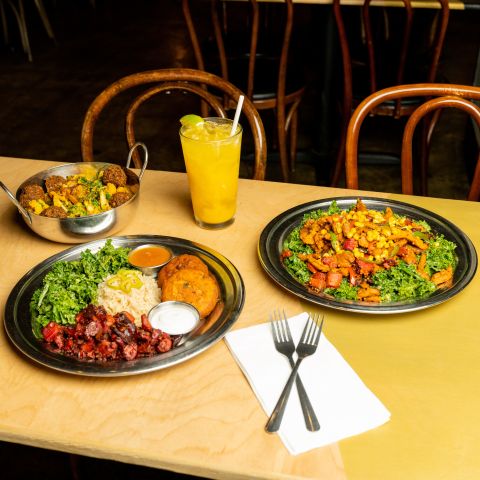 several plates of Indian food and an iced orange drink atop a wooden restaurant table