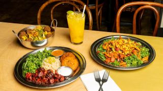 Several plates of Indian food on top of a wooden restaurant table with an iced orange drink.