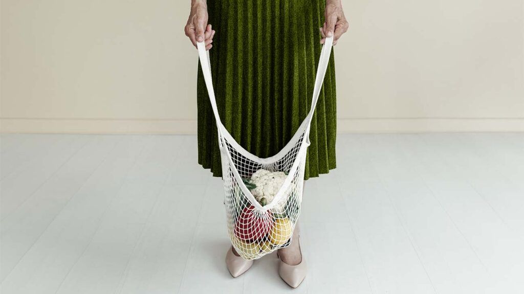 close-up of hands holding a white mesh bag filled with vegetables against their emerald green skirt