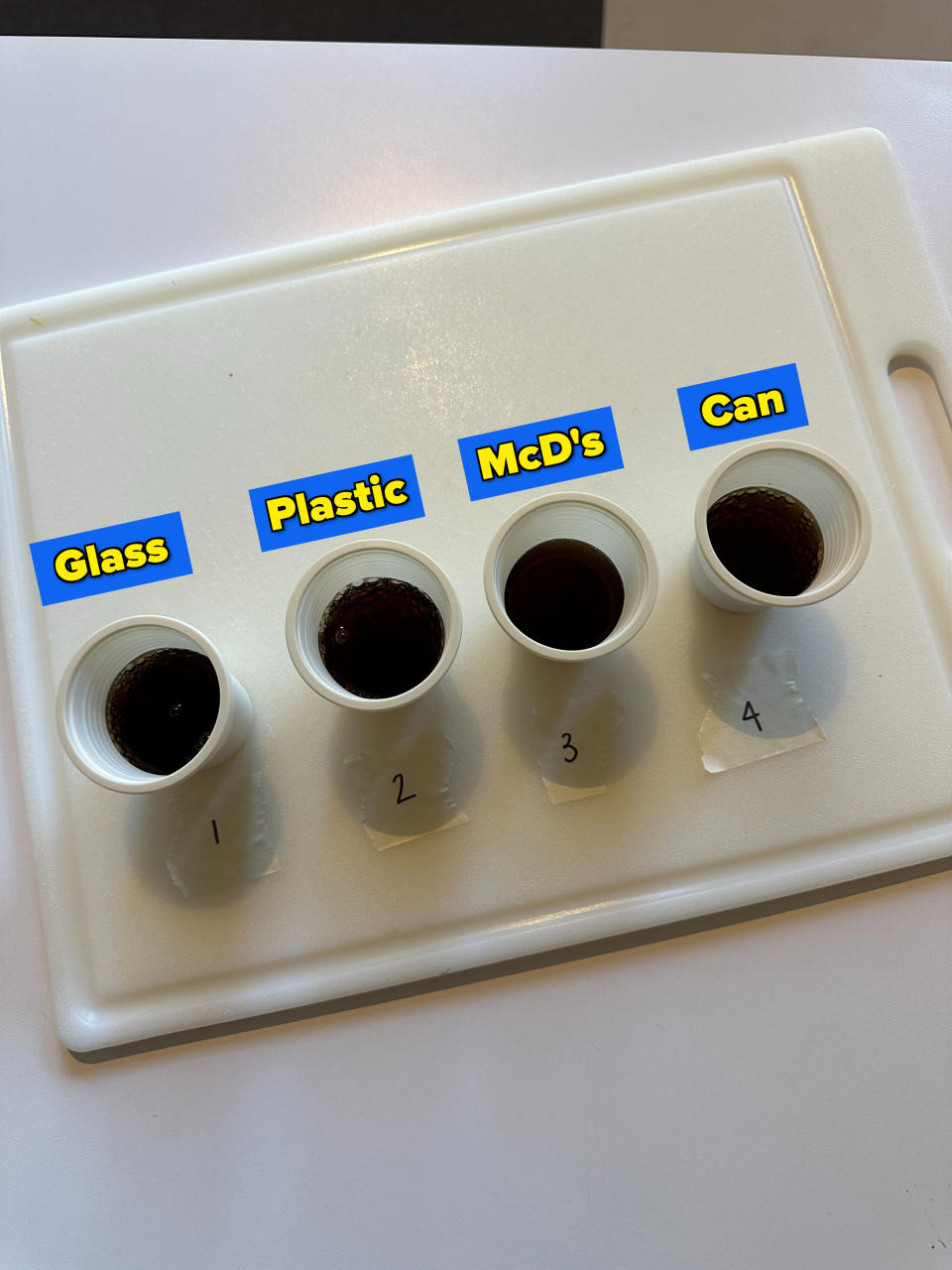 four mouthwash cups on a cutting board, each filled with diet coke