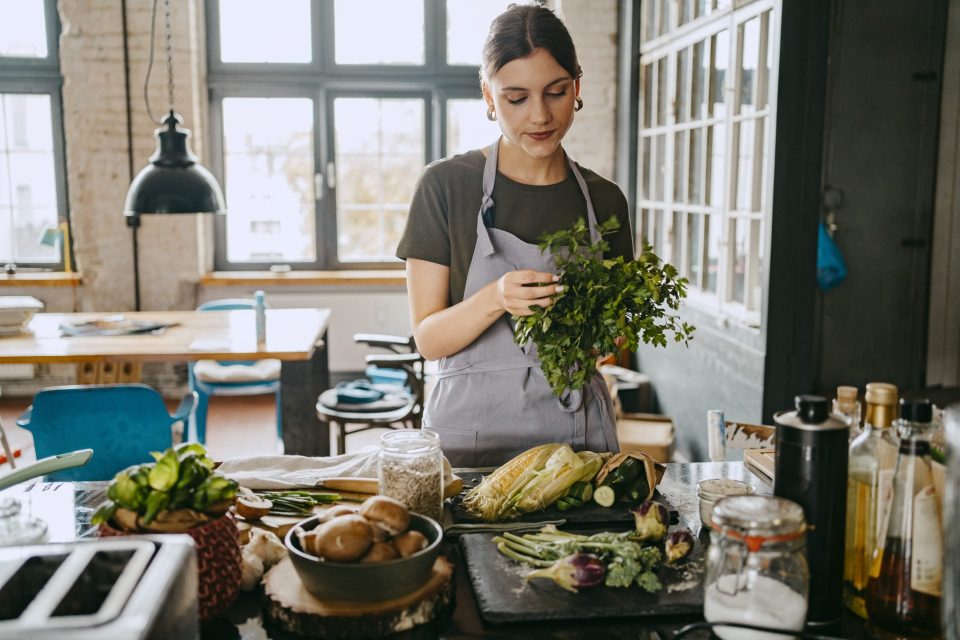 Female chef wearing apron doing quality check of cilantro standing in studio kitchen