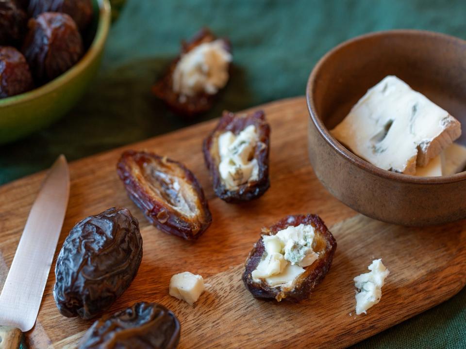 sliced dates stuffed with hunks of blue cheese on a cutting board surrounded by the ingredients