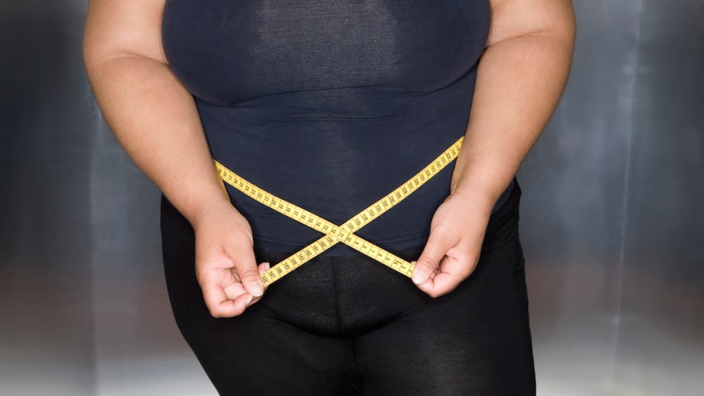 Woman measures her waist size with measuring tape.