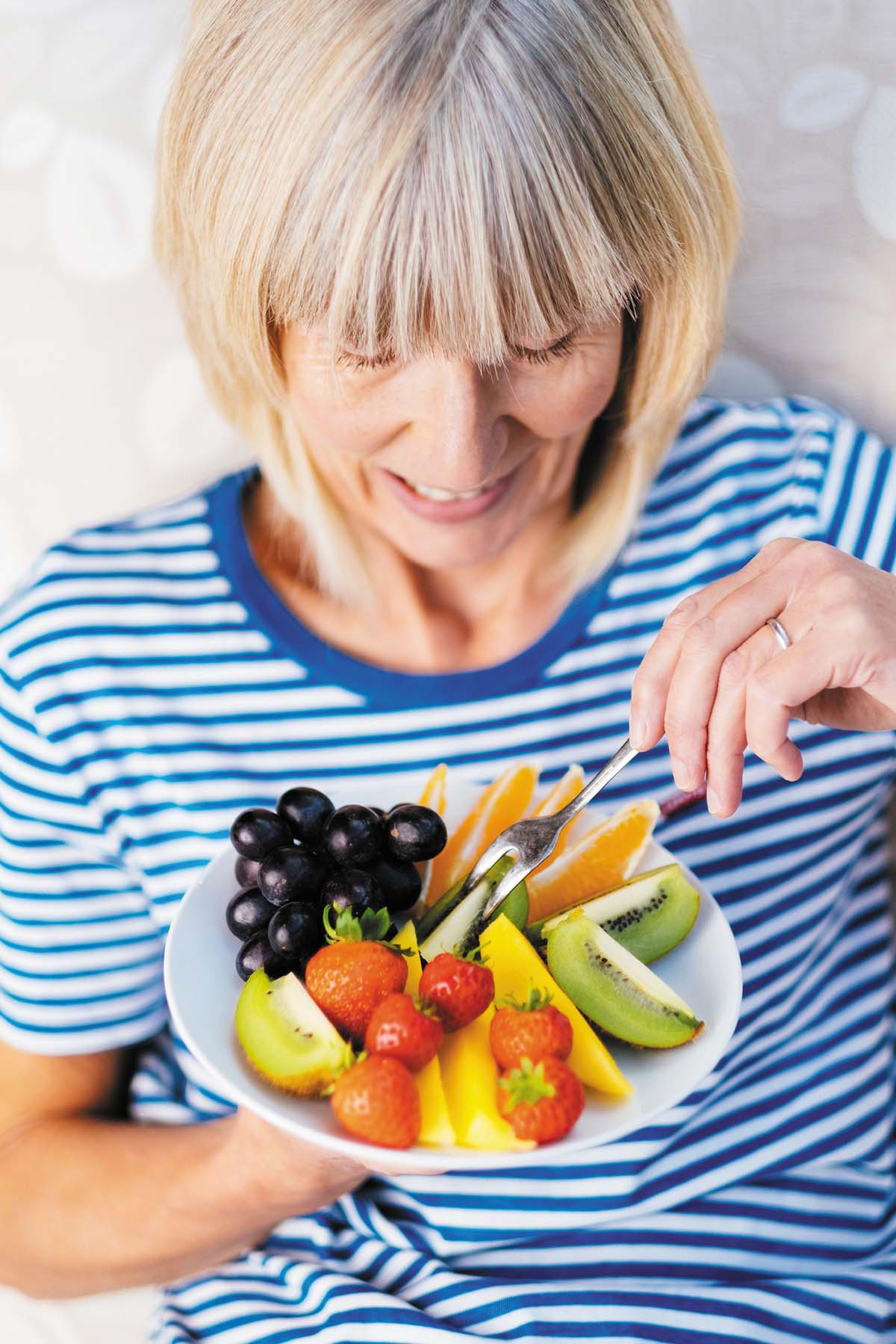 photo of a woman holding a plate containing an assortment of fruit, and a fork in her other hand