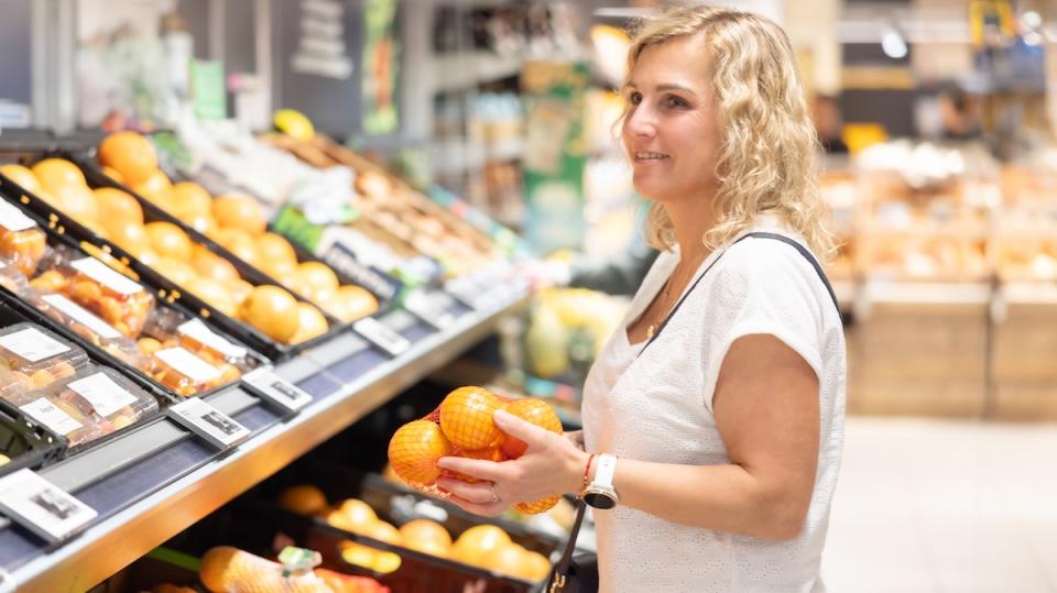 A woman buys groceries with a shopping cart. A young brunette buys fruit in a supermarket.