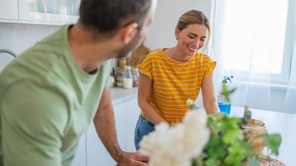 Photo of young married couple cleaning kitchen counter. Husband is involved in cleaning duties. Focus on woman.