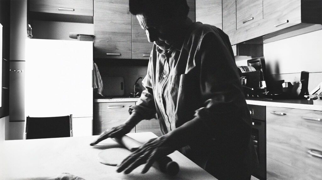 black and white photo of older person stretching dough with a rolling pin