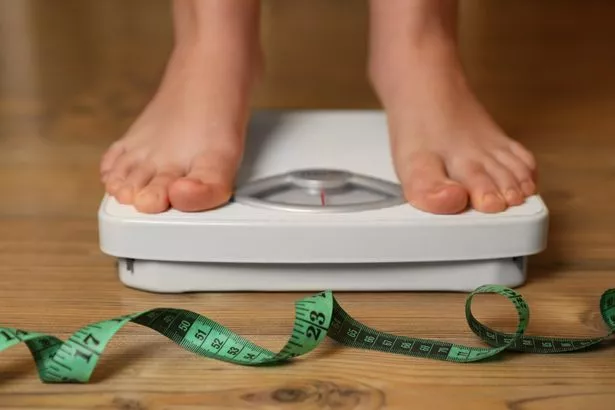 Overweight girl using scales near measuring tape on wooden floor, closeup